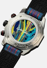 Orologio cronografo con un quadrante rotondo blu e giallo a motivo, cassa in acciaio inossidabile e cinturino in gomma nera con dettagli in tessuto colorato.
