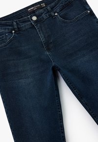 Tummansiniset farkut slim fit -tyylissä, joissa on viisi taskua, metallinen nappikiinnitys ja hienovarainen tekstuuri.