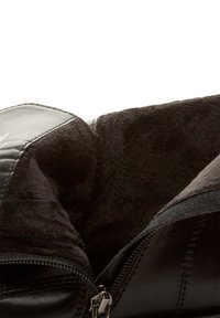 Crna kožna torba s mekim, teksturiranim crnim unutrašnjim postavom. Ima zatvarač i ukrasne šavove uz rubove.