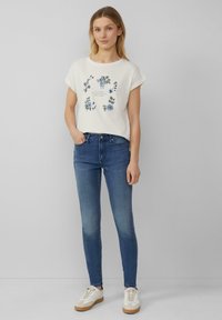 Chemise blanche à manches courtes avec imprimé floral, associée à un jean en denim bleu ajusté et des baskets blanches avec des accents beige. Design minimaliste.