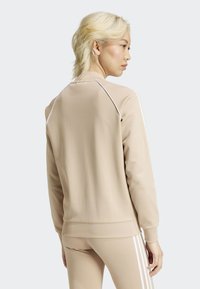 Sudadera beige con puños y dobladillo acanalados, con detalles de acento en blanco y un cuello redondo, hecha de una tela suave.