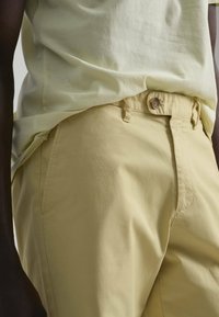 Pantalones de algodón amarillo claro con textura suave, que cuentan con un cierre de botón y bolsillos laterales, combinados con una camisa amarilla clara.