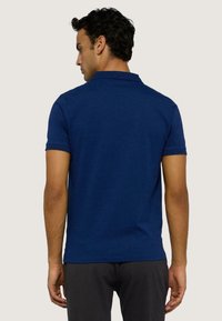 Polo shirt bleu marine en tissu doux, avec des manches courtes, un col classique et un design uni. La vue arrière montre une coupe ajustée.