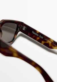 Sonnenbrille aus Schildpatt mit dunklen Gläsern und dickem Rahmen. "Massimo Dutti" ist auf dem Bügel eingraviert, zusammen mit Modellnummern.