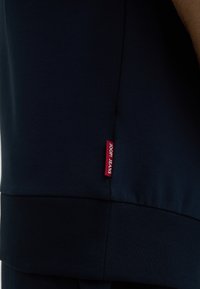 Donkerblauwe sweatshirt met een gladde textuur, voorzien van een rode "JOOPI JEANS" label aan de linkerkant nabij de zoom.