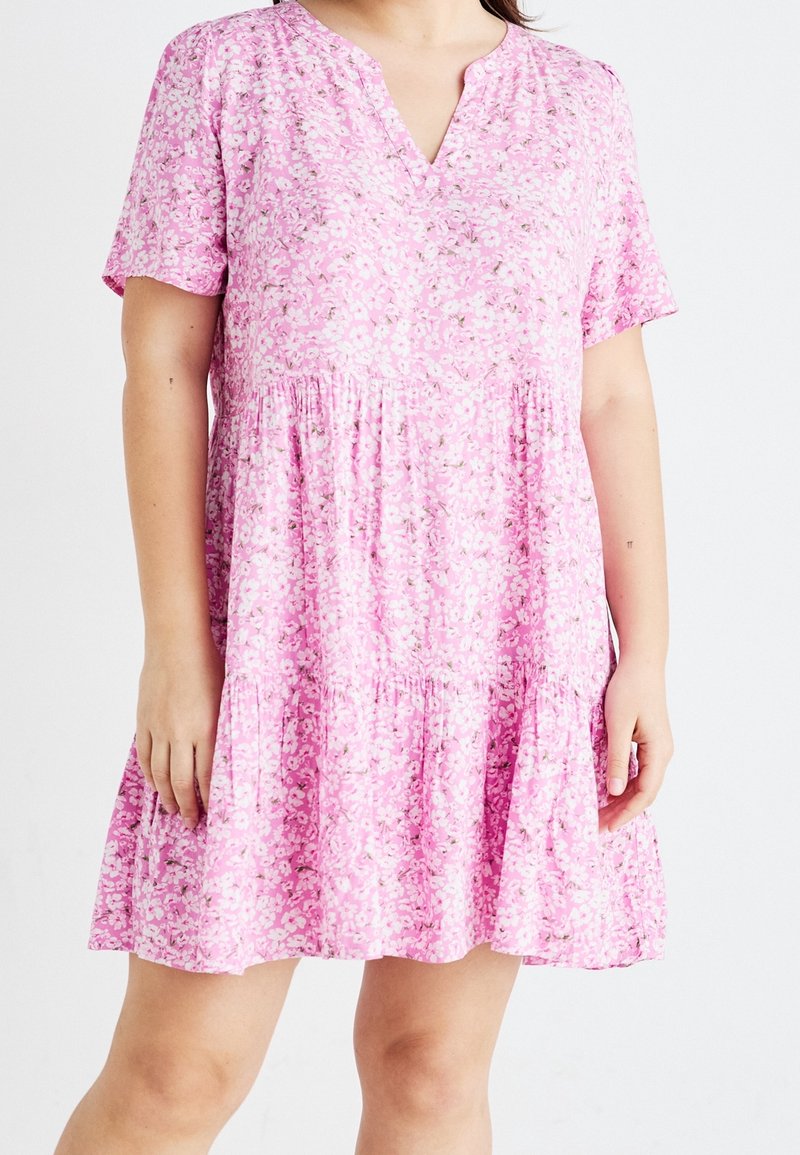 Růžové květinové šaty s krátkými rukávy, výstřihem do V a nabranými volány. Vyrobené z lehké texturované látky s malými bílými a zelenými květinovými vzory.