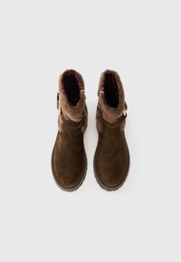 Un par de botas de ante marrón hasta el tobillo con forro de piel de pelo y detalle de hebilla dorada, vistas desde arriba sobre un fondo blanco.