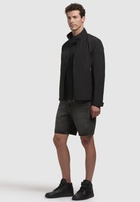 Black zip-up jacket with a high collar, paired with dark denim shorts and black high-top sneakers, showcasing a casual look.