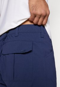 Pantalones cortos azul marino con cintura elástica, con bolsillos laterales y traseros, y detalles de costuras en contraste. Textura suave, diseño casual.