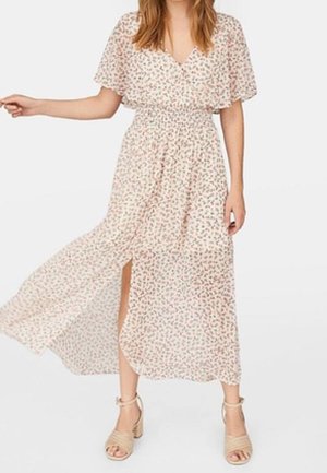 Frau trägt ein leichtes, florales Midikleid mit Flügelärmeln und einem vorderen Schlitz, kombiniert mit beigen Sandalen mit Blockabsatz.