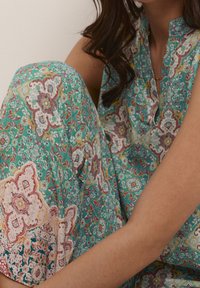 Sleeveless turquoise floral dress featuring intricate patterns in pink, yellow, and white, with a slightly ruffled neckline and soft texture.