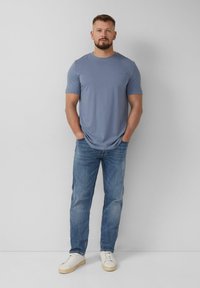 Lichtblauw T-shirt met korte mouwen, relaxed fit; gecombineerd met middelblauwe jeans en witte sneakers. De stof lijkt glad, met minimale details.