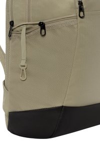 Mochila beige con textura de malla y dos bolsillos con cremallera, con un fondo negro sólido. Correas ajustables y un acabado mate.