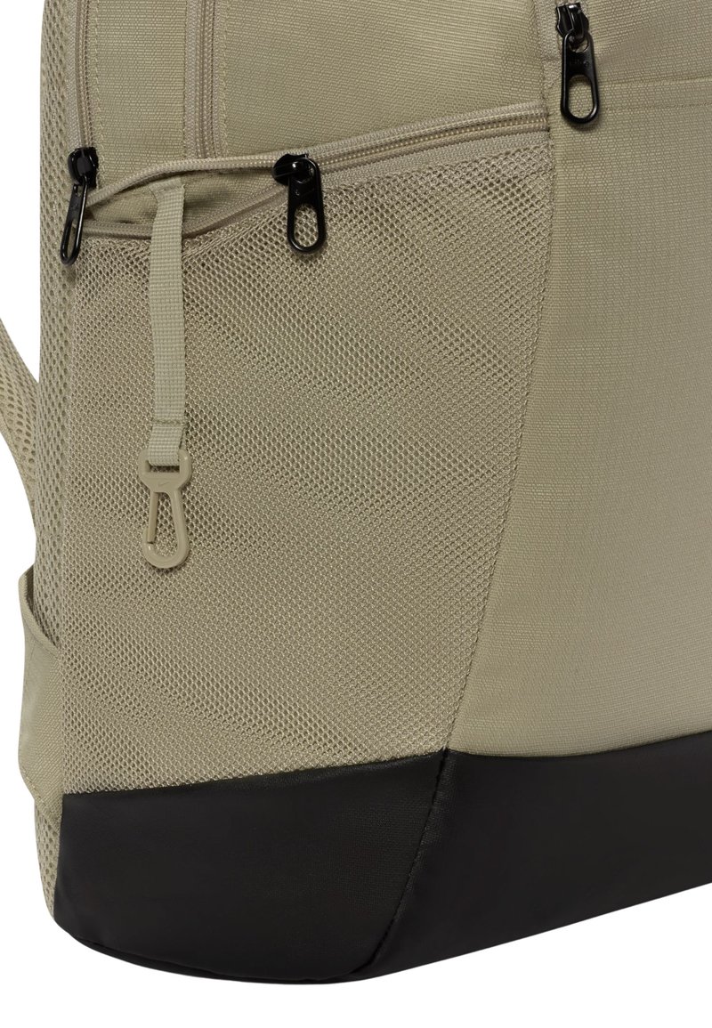 Beige ryggsäck med nätstruktur och två dragkedjefickor, med en solid svart botten. Justerbara axelremmar och en matt yta.