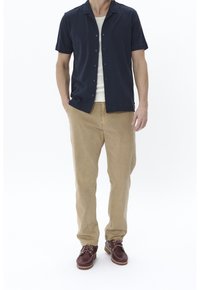 Marinblå kortärmad skjorta med knappar över en vit linne, kombinerat med beige byxor och bruna snörskor med krämfärgade sulor.