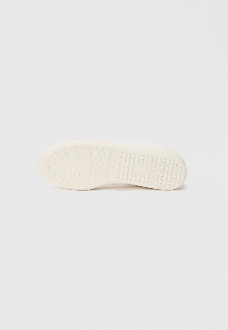Suola della scarpa in gomma color avorio con una superficie testurizzata che presenta motivi circolari e triangolari per aderenza e supporto.