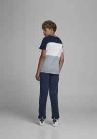 T-shirt a maniche corte in blocchi di colore navy, bianco e grigio, abbinato a pantaloni felpati navy e sneaker bianche con dettagli neri.