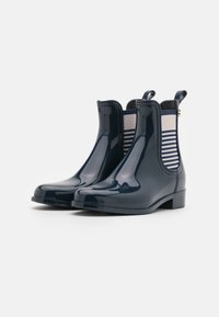 Botas de tobillo de goma brillantes en color navy, con paneles laterales elásticos a rayas y pequeñas lengüetas, que cuentan con un tacón bajo y cuadrado.