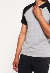 Polo gris avec un design de manches raglan noires. Caractérisé par un col classique, une texture douce et une silhouette ajustée.