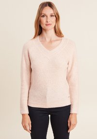 Helles rosa Strickpullover mit V-Ausschnitt, langen Ärmeln und dezenten funkelnden Akzenten. Strukturiertes Detail entlang des Ausschnitts und dem Saum.