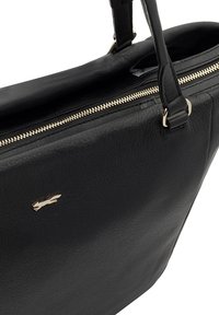 Zwarte leren tote bag met een gestructureerde afwerking, voorzien van een gouden rits en een klein metallic logo aan de voorkant. Afneembare handvatten inbegrepen.