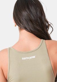 Olivgrünes, geripptes Tanktop mit rundem Ausschnitt und weißem Logo-Druck auf dem Rücken. Weicher Stoff und figurnahe Passform.