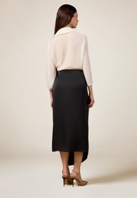 Helle Creme-Bluse mit durchsichtigen Ärmeln, kombiniert mit einem taillierten schwarzen Satinrock. Dazu gehören schicke Sandalen mit Absatz. Einfaches, elegantes Design.