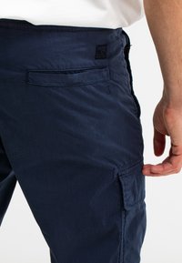 Marineblauwe cargobroeken van lichtgewicht materiaal, met zijzakken, een achterzak en een subtiele merketiket op de tailleband.