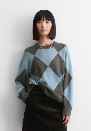 Pullover in Hellblau und Dunkelgrau mit einem Rautenmuster, ausgestattet mit einem Rundhalsausschnitt, langen Ärmeln und einem lockeren Schnitt, kombiniert mit einem schwarzen Rock.