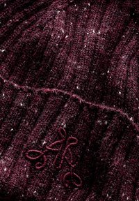 Gebreide bordeauxrode beanie met een geribbelde textuur, voorzien van witte spikkels en een groot geborduurd monogramdetail in dezelfde kleur.