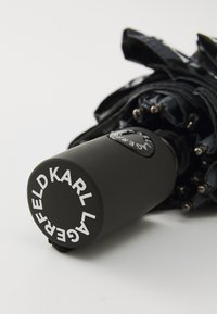 Black umbrella with a smooth, matte handle featuring white lettering "KARL LAGERFELD." Folded canopy shows textured fabric and metallic ribs.