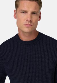 Maglione a coste blu navy con scollatura a girocollo. Caratterizzato da una consistenza in maglia spessa e una silhouette aderente. Senza loghi o decorazioni visibili.