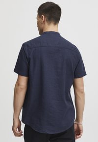 Marineblaues Leinenhemd mit kurzen Ärmeln, abgerundetem Saum und Rückenpasse. Verfügt über einen Stehkragen und eine glatte Stoffoberfläche.