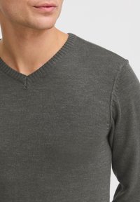 Pull en tricot gris avec un col en V, présentant des détails en maille côtelée au niveau du cou et des poignets, une texture lisse et un design ajusté.