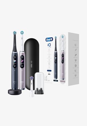 Zwei Oral-B iO elektrische Zahnbürsten, eine schwarze und eine weiße, mit Ladestation, Reiseetui, extra Bürstenkopf und Produktverpackung.