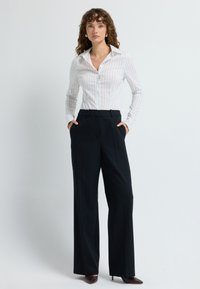 Biała koszula z długim rękawem w pionowe paski z kołnierzykiem, połączona z czarnymi spodniami o wysokim stanie z dopasowanym krojem i bocznymi kieszeniami.