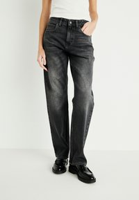 Zwarte denim jeans in een relaxed fit, met een vijf-pocket ontwerp, hoge taille en subtiele vervaging. Gecombineerd met zwarte schoenen.