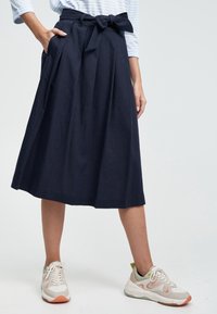 Marinblå kjol i knälängd med veck och knytning i midjan. Matchad med ljusa sneakers. Slät tygkvalitet, avslappnad design.