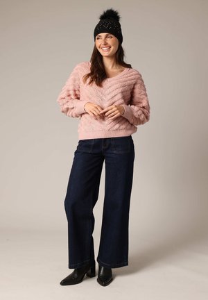 Pull en tricot rose avec un motif en zigzag, associé à un jean large bleu foncé et des bottines à talons noires. Bonnet noir avec pompon.