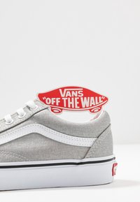 Šedé plátěné tenisky s bílými akcenty, které mají výrazný vlnový design. Černý pruh na podešvi a červená nášivka "Vans" na zadní straně.