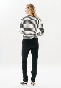 Black skinny jeans paired with a white and black striped ribbed long-sleeve top, displayed from the back, highlighting fit and texture.