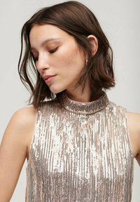 Top sin mangas en rosa dorado con cuello alto, que presenta patrones de lentejuelas verticales y una textura suave.