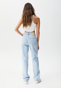 Jeans bleu clair taille haute avec une coupe décontractée, dotés de deux poches arrière et d'une étiquette carrée à la taille. Portés avec un crop top blanc.