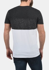 Kortærmet t-shirt med farveblokdesign: øverste sektion med sorte spidser, nederste sektion i hvid, lavet af blød bomuldsstof.