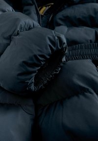 Melnas pūsta jakas audums ar gludu ārējo tekstūru un elastīgu aproci. Iespējas ar izšuvuma dizainu un mīkstu pildījumu siltumizolācijai.