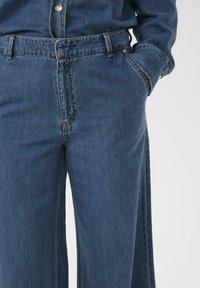 Dark blue denim jeans with a relaxed fit, featuring a button and zipper closure, belt loops, and side pockets. Smooth texture.