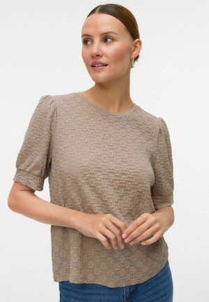 Blouse à manches courtes de couleur marron clair avec un col rond et des manches bouffantes douces, associée à un jean en denim bleu.