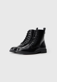 Botas de cuero negro hasta el tobillo con punta redonda, cordones en la parte frontal y tira en el talón. Presentan una textura suave y una suela de goma resistente.