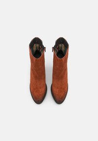 Bottes cheville en daim orange brûlé avec un bout pointu et une semelle noire. Intérieur avec une doublure en tissu à rayures. Fermeture éclair à l'arrière.