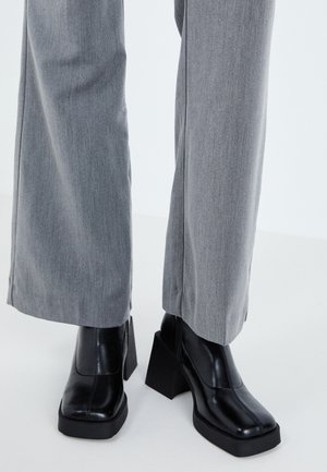 Zwarte hoge laars met een vierkant teen, een zachte leren afwerking en een chunky platform. Gecombineerd met lichtgrijze, wijde broeken.